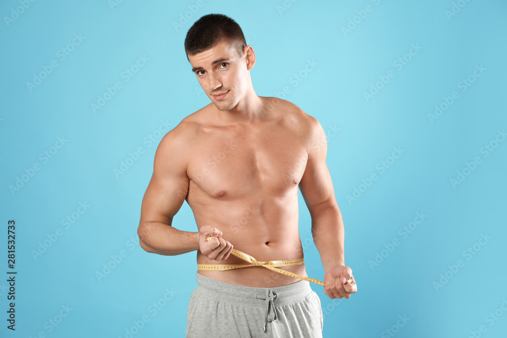 Young man with slim body using measuring tape on light blue background