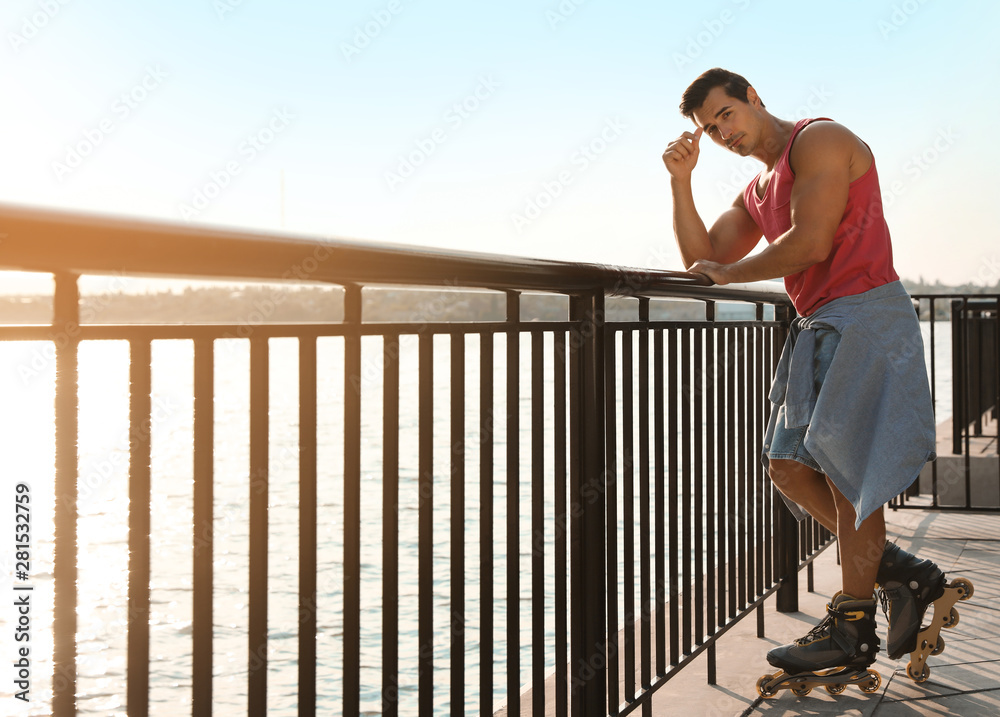 Handsome young man with roller skates on pier near river, space for text