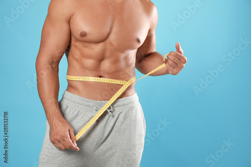 Young man with slim body using measuring tape on light blue background, closeup view. Space for text