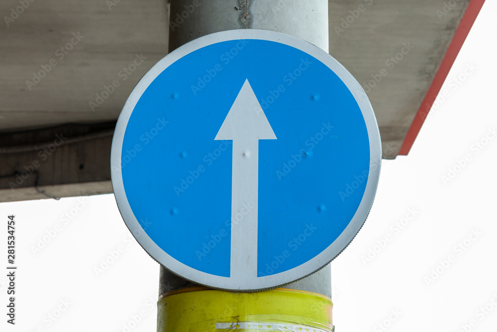 White arrow on blue background of round traffic sign. An entry-inhibiting sign is attached to a pole. Blue road sign, indicates the mandatory direction of traffic.