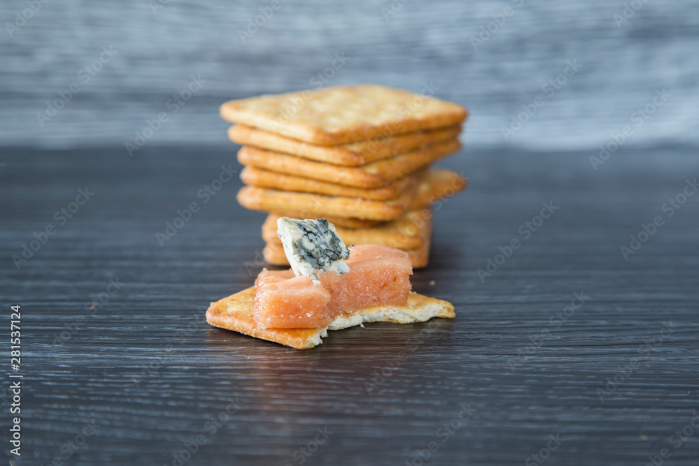 Delicious homemade quince paste served with creamy blue vein cheese and wheat crackers. On a dark background, nice contrast. Great combination of sharp cheese with sweet paste on a salty cracker.