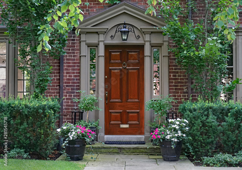 front door of older brick house with shady garden and flower pots Fototapet
