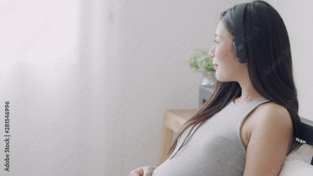 Pregnant Asian mother open music for their children using headphone in the bedroom. Pregnant Asian mother open music for their children using headphone in the bedroom.