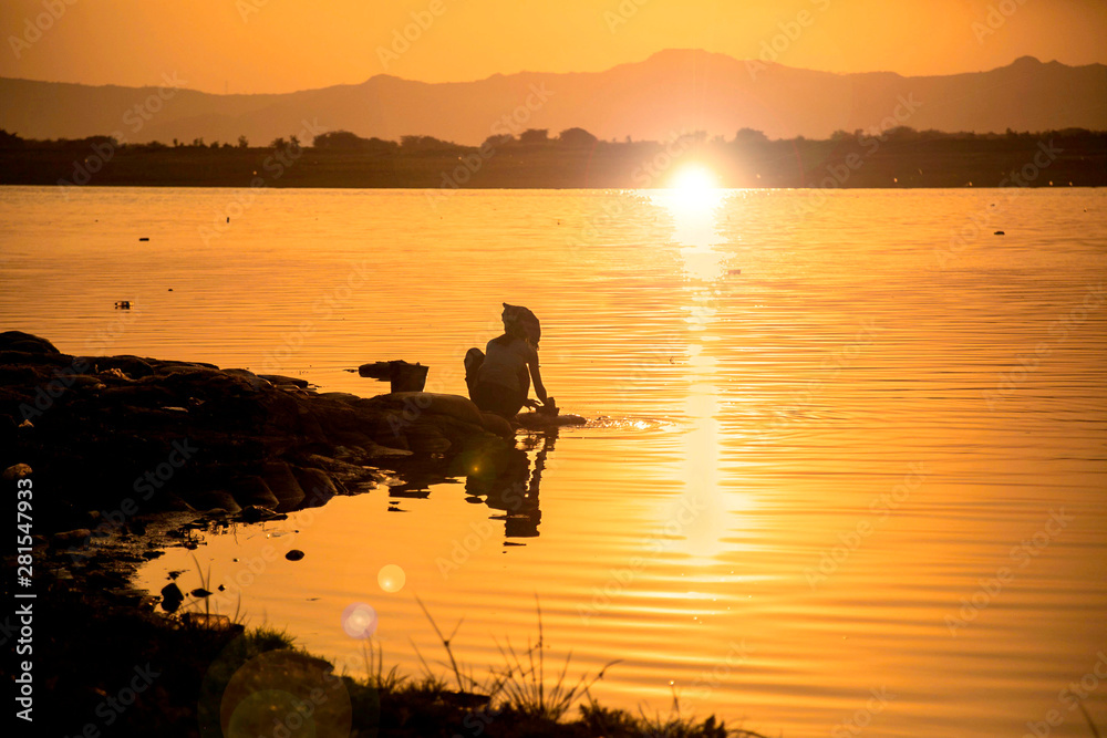 Silhouette woman washing clothes in the lake at sunset in Bagan, Myanmar Silhouette woman washing clothes in the lake at sunset in Bagan, Myanmar
