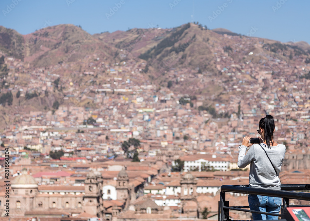 A tourist woman takes a picture of Cusco's city from the San Blas viewpoint.