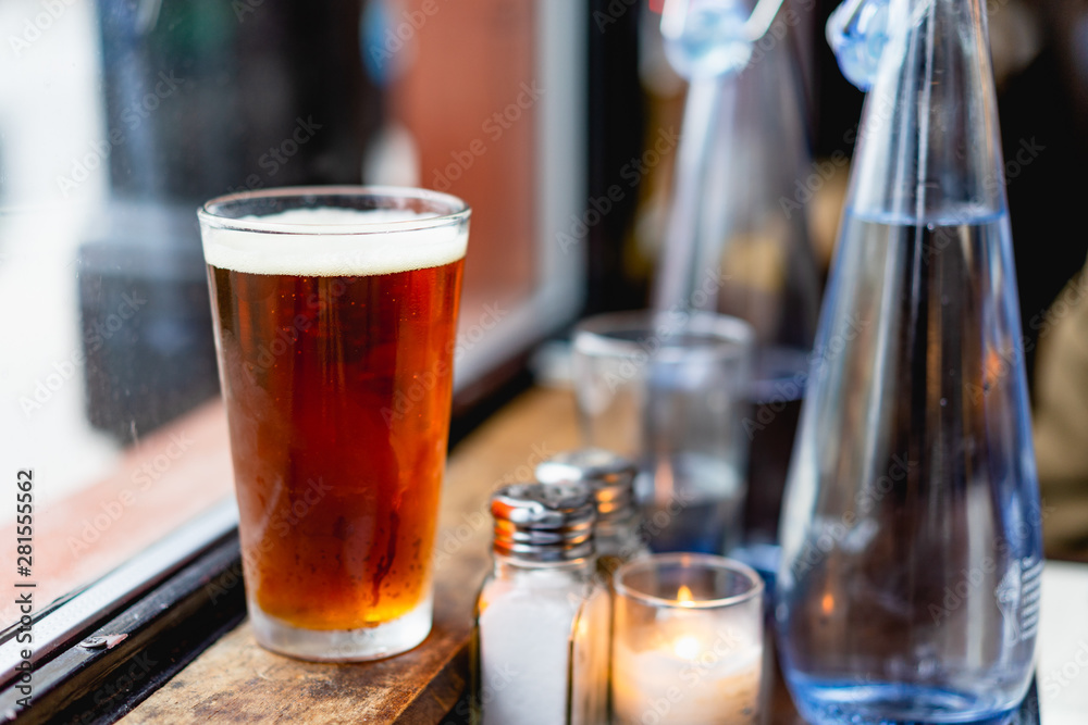 IPA beer next to a window at a rustic bar next to bottles and glasses of water IPA beer next to a window at a rustic bar next to bottles and glasses of water