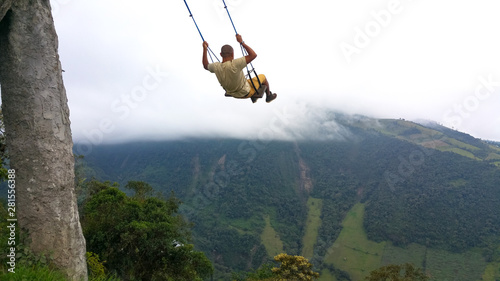 Young man having fun on the swing at the end of the world located at Casa Del Arbol, The Tree House in Banos, Ecuador