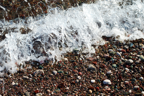 white transparent ocean wave on the beach with borwn pebbels and sand photo