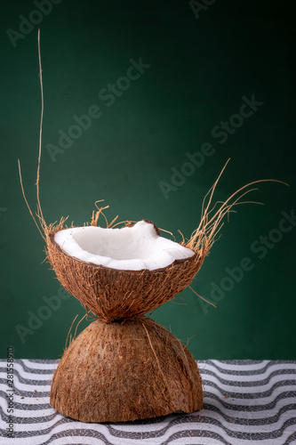 Coconut halves forming a chalice with the outer brown shell and inner white coco on a pattern surface against a dark green background with hairs sticking out. Studio concept of a natural cocktail cup. photo