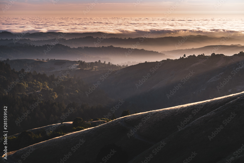 Sunset view of layered hills and valleys covered by a sea of clouds in Santa Cruz mountains ; San Francisco bay area, California Sunset view of layered hills and valleys covered by a sea of clouds in Santa Cruz mountains ; San Francisco bay area, California
