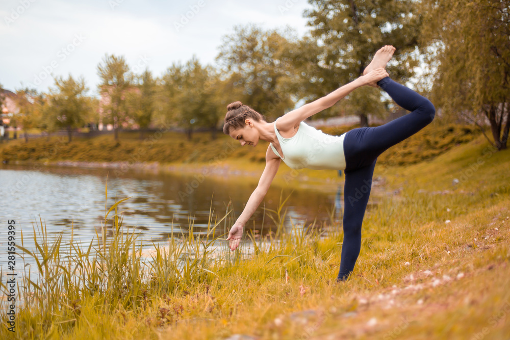 Slim brunette girl goes in for sports and performs yoga poses in the fall in nature by the lake Slim brunette girl goes in for sports and performs yoga poses in the fall in nature by the lake
