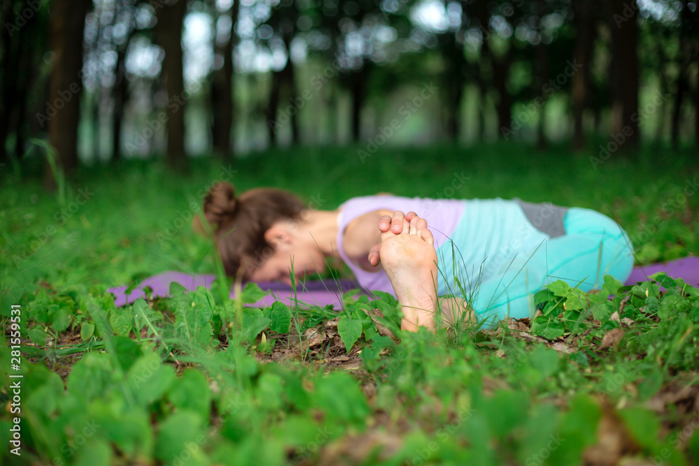 Thin brunette girl plays sports and performs beautiful and sophisticated yoga poses in a summer park. Green lush forest on the background. Woman doing exercises on a yoga mat Thin brunette girl plays sports and performs beautiful and sophisticated yoga poses in a summer park. Green lush forest on the background. Woman doing exercises on a yoga mat