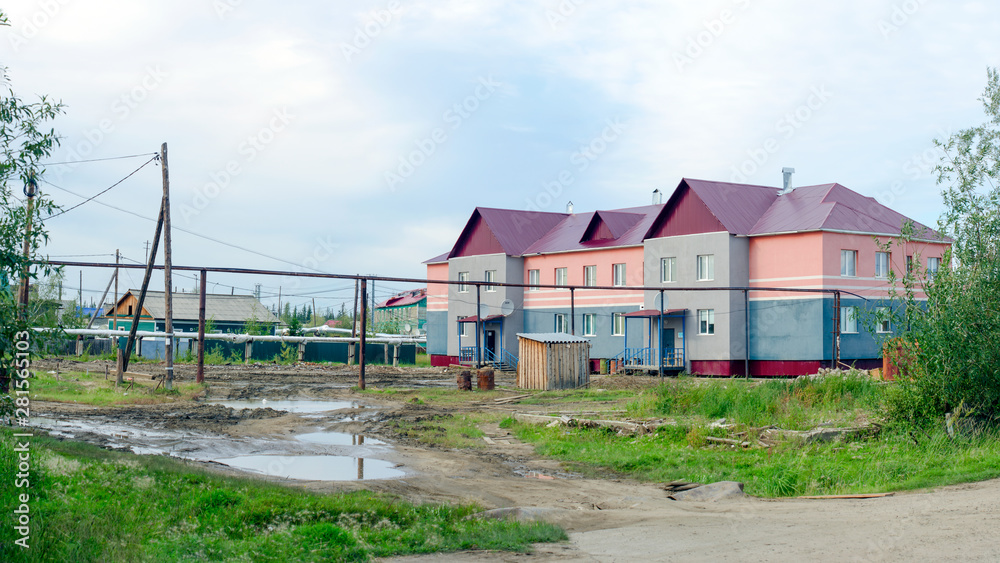 Apartment building in the Northern settlement of Yakutia, Suntar next to the dirty road and the puddles are made of wood and a toilet on the street.