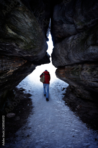 A man with a backpack out of the dark snow-cavern in the bright light.