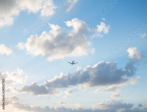 Flying plane in the sky with clouds at sunset as a background