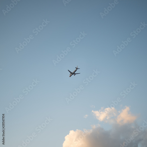 Flying plane in the sky with clouds at sunset as a background