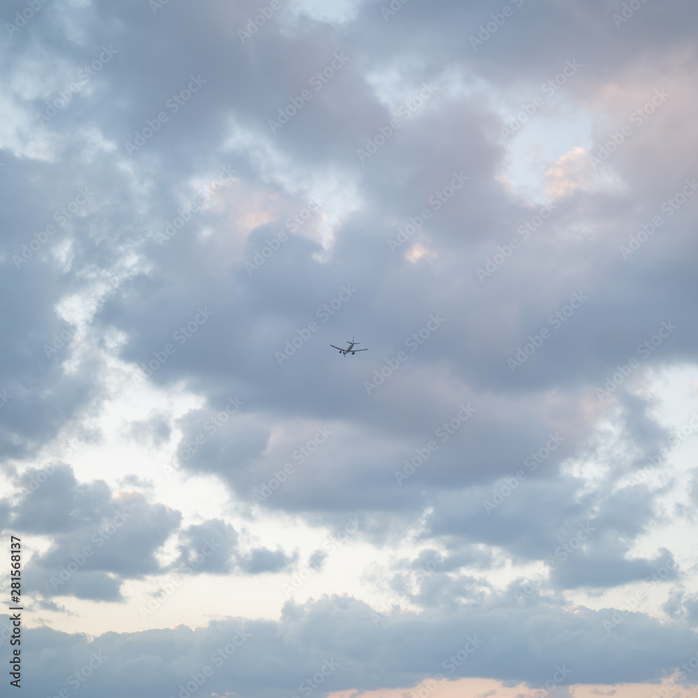 Flying plane in the sky with clouds at sunset as a background