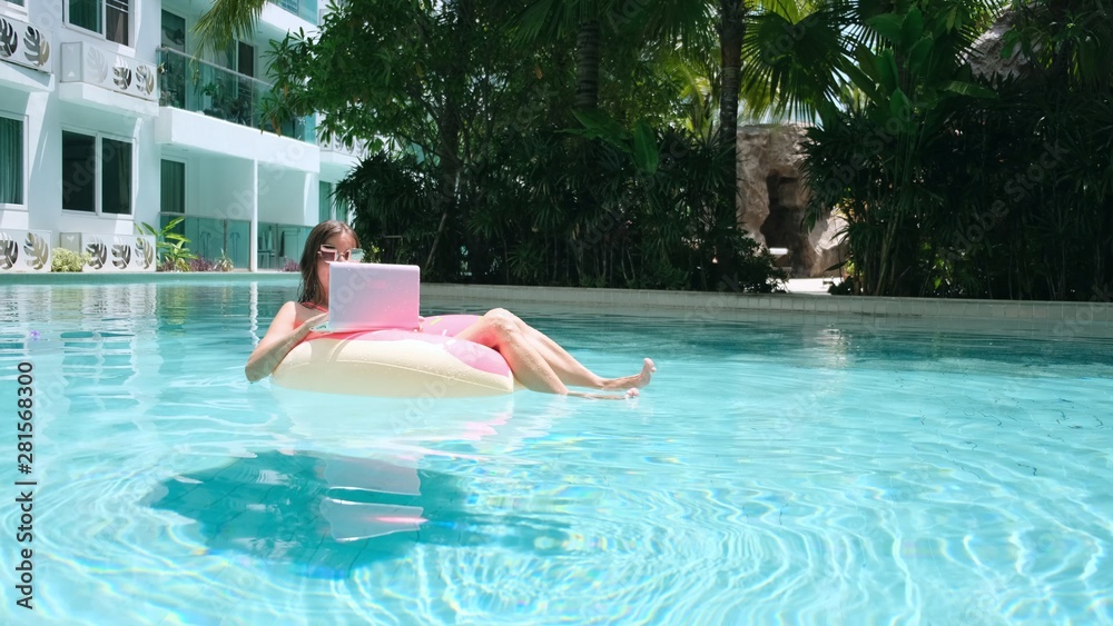 young woman swims in the sea in a swimming circle. Girl resting in the pool on an inflatable circle with a computer, top view