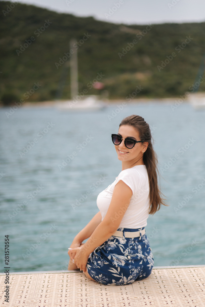 Attractive stylish woman on the pier by the sea. Beautiful inflow surrounded by mountains