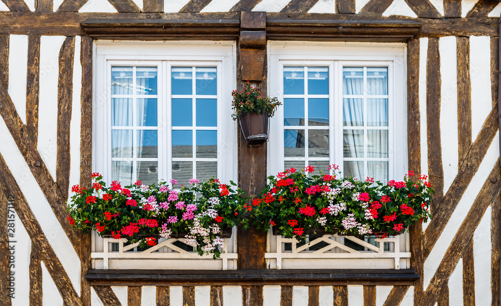 Two windows in a half-timbered house decorated with the flowers outside. Normandy, France.