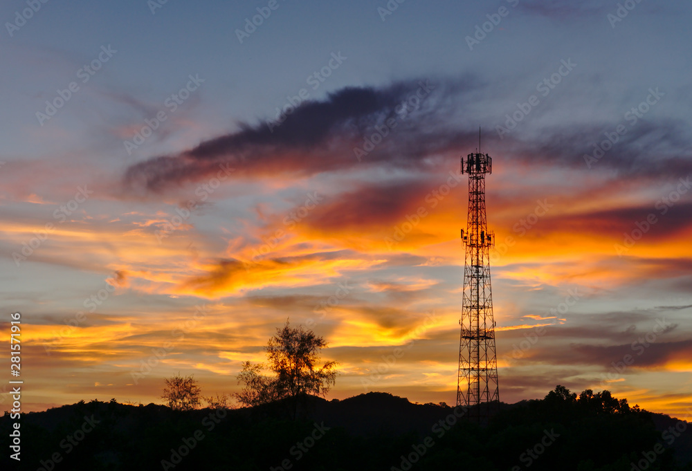 Tall mobile cell phone tower on the high hill sending signal to connect people around the world in the evening when sunset with orange red sky and clouds with copy space on the left..