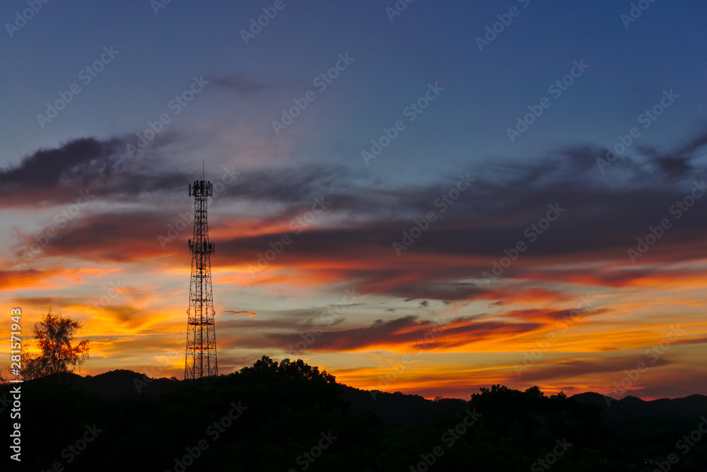 Tall mobile cell phone tower on the high hill sending signal to connect people around the world in the evening when sunset with orange red sky and clouds with copy space on the right. Tall mobile cell phone tower on the high hill sending signal to connect people around the world in the evening when sunset with orange red sky and clouds with copy space on the right.