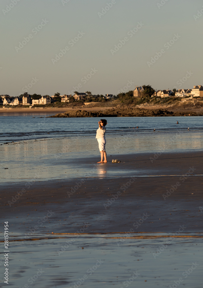Obraz premium A woman practicing yoga on the beach of Saint Malo in the glow of the setting sun. Brittany, France