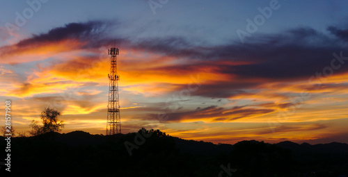 Fototapeta Naklejka Na Ścianę i Meble -  Panorama shot of Tall mobile cell phone tower on the high hill sending signal to connect people around the world in the evening when sunset with orange red sky and clouds with copy space on the right.