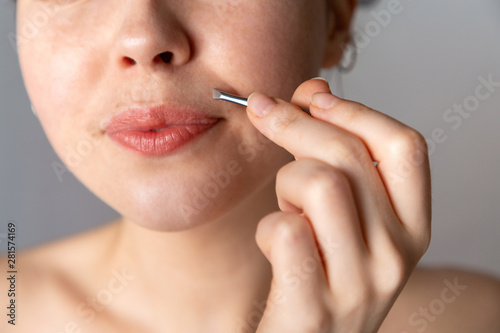 A young woman plucks her hair over her upper lip with tweezers. The concept of getting rid of unwanted facial hair. Close up photo