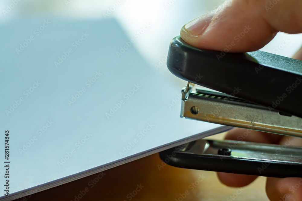 Woman's right hand holding stapler and stapling white paper on wooden background, Close up & Macro shot, Selective focus, Office Stationery concept Woman's right hand holding stapler and stapling white paper on wooden background, Close up & Macro shot, Selective focus, Office Stationery concept