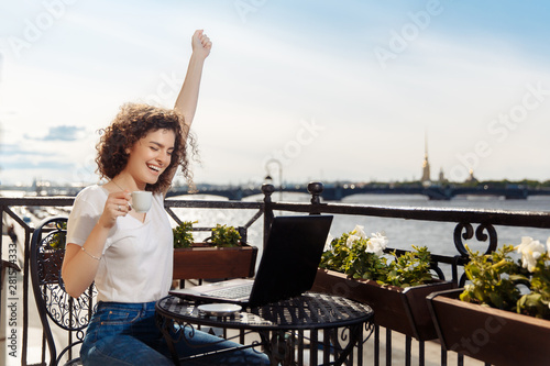 Cute happy young girl working on computer and smiling. Beautiful woman with laptop on a balcony with a landscape on the river Neva and the city of St. ..Petersburg