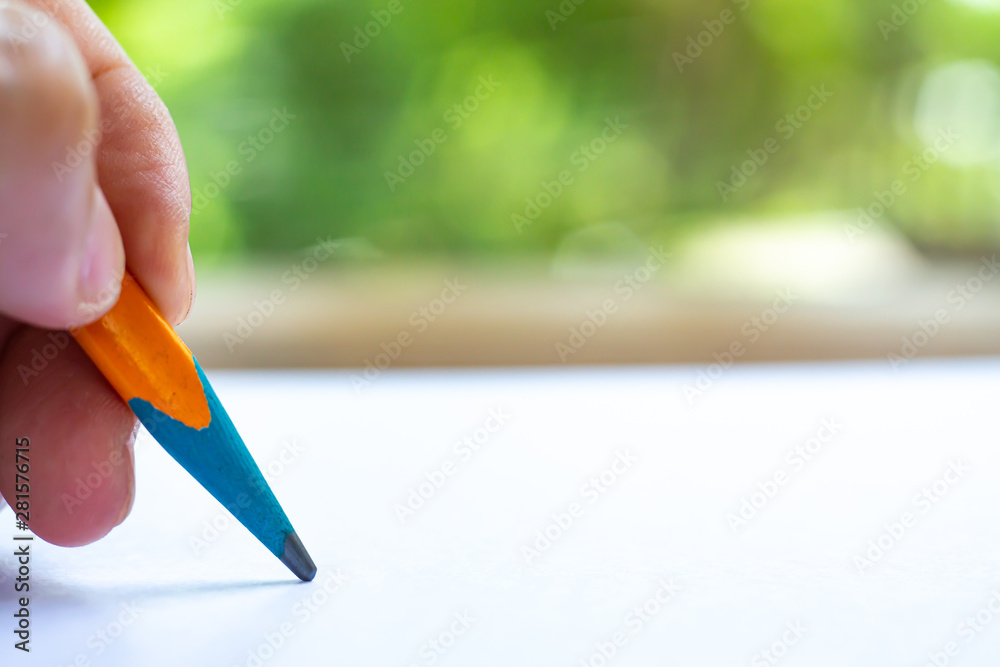 Woman's left Hand holding multicoloured pencil, writing letter on white paper, Bokeh green garden background, Notebook, Close up & Macro shot, Selective focus, Communication, Stationery concept Woman's left Hand holding multicoloured pencil, writing letter on white paper, Bokeh green garden background, Notebook, Close up & Macro shot, Selective focus, Communication, Stationery concept