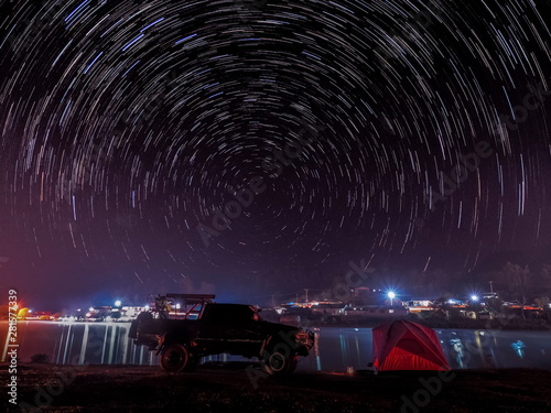 Lake view at night of a 4WD. Truck and a camping tent on the bank of reservoir with soft mist and star Trails in night sky background  camping at Ban Rak Thai Reservoir  Mae Hong Son  Thailand.