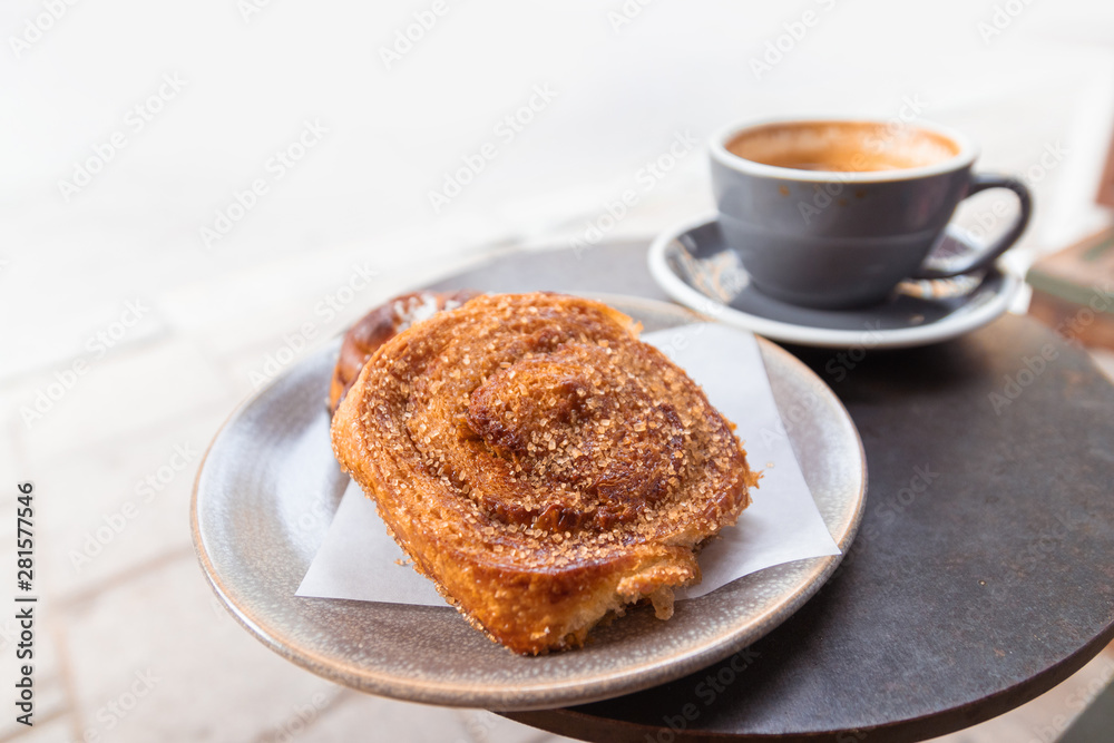 Warm cinnamon bun with icing sugar with cup of coffee Warm cinnamon bun with icing sugar with cup of coffee