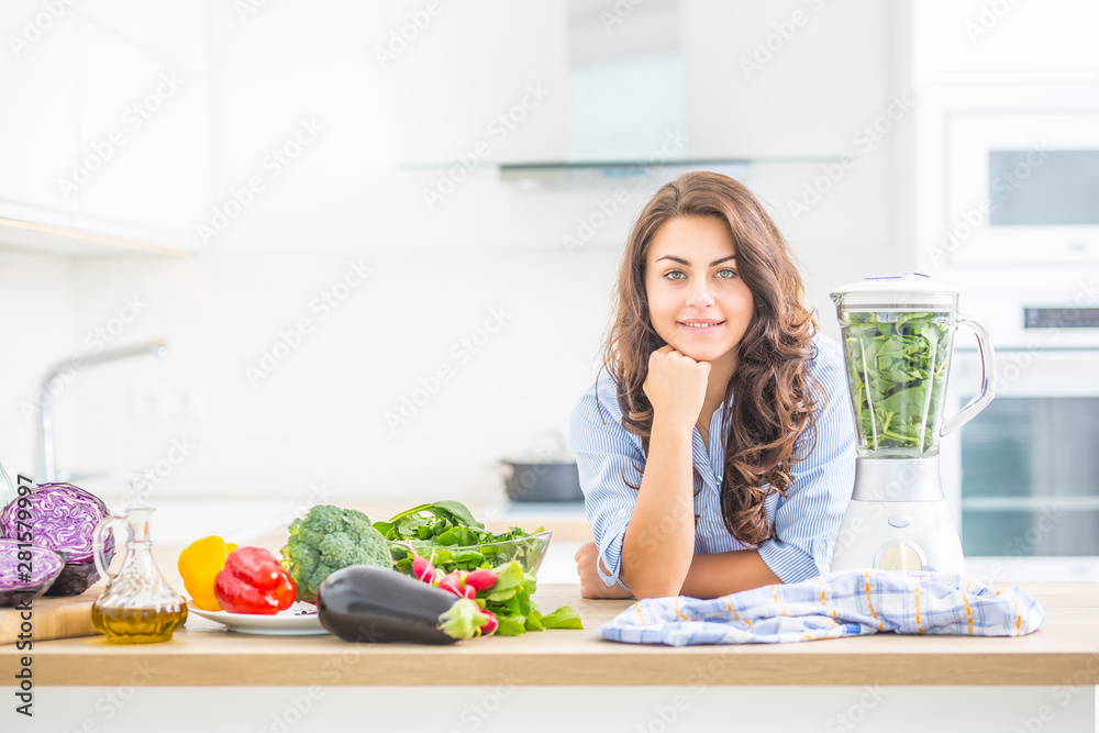 Woman making vegetable soup or smoothies with blender in her kitchen. Young happy woman preparing healthy drink with spinach broccoli arugula and other vegetable. Woman making vegetable soup or smoothies with blender in her kitchen. Young happy woman preparing healthy drink with spinach broccoli arugula and other vegetable.
