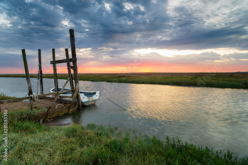 Sunrise over a boat moored to an old wooden jetty at Thornham