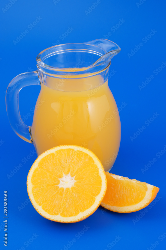 Orange juice in pitcher with orange fruit slices on blue background Orange juice in pitcher with orange fruit slices on blue background