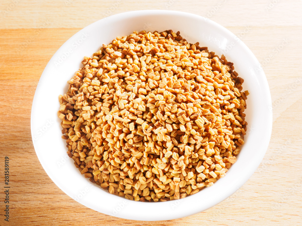 Fenugreek (Trigonella) in white ceramic cup on a wooden background Fenugreek (Trigonella) in white ceramic cup on a wooden background