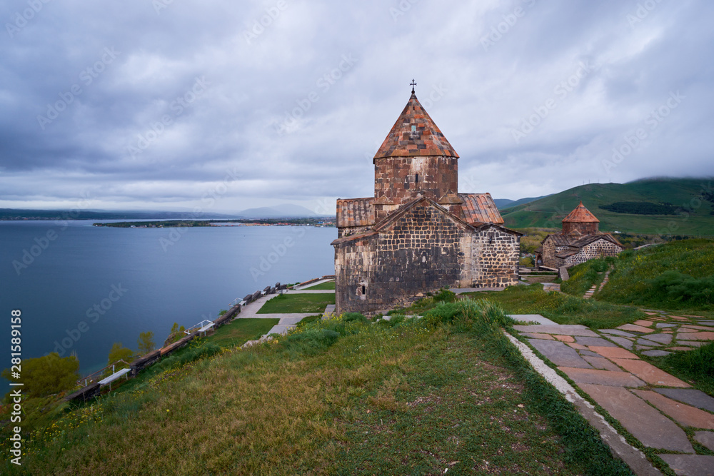The ancient monastery is located on top of the endless water expanses of the Lake Sevan on an overcast day with clouds in the sky.