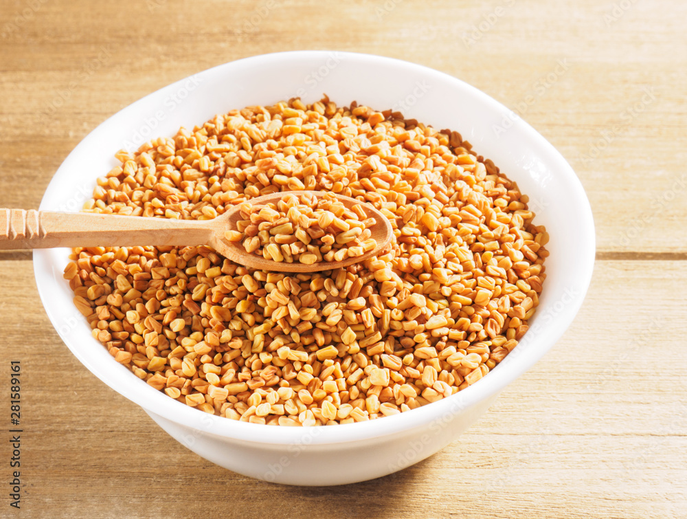 Fenugreek (Trigonella) in a ceramic white cup with spoon on a wooden background Fenugreek (Trigonella) in a ceramic white cup with spoon on a wooden background