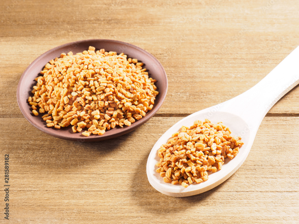 Fenugreek (Trigonella) in a clay plate with spoon on a wooden background Fenugreek (Trigonella) in a clay plate with spoon on a wooden background