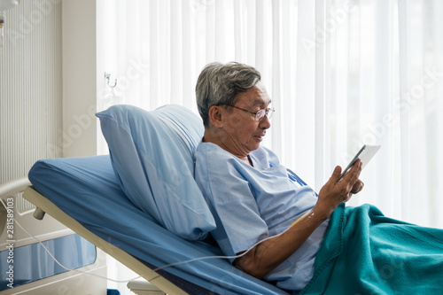 Happy elderly patient sitting on bed and making video call with tablet at hospital.