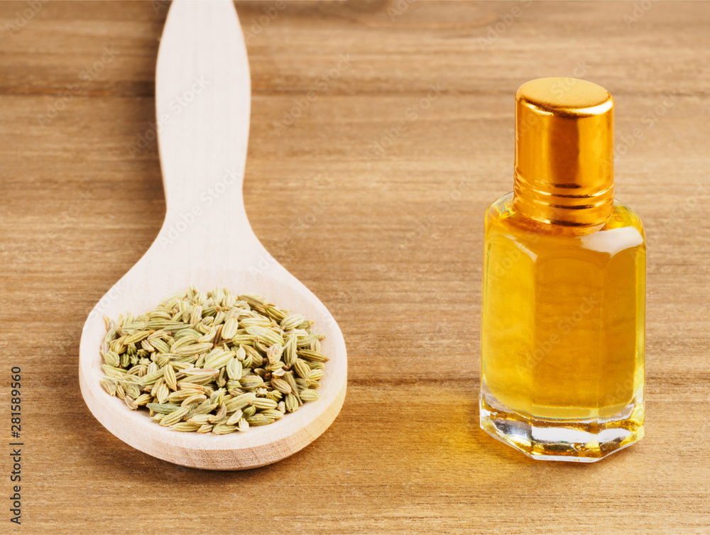 Fennel seeds (Foeniculum vulgare) in wooden spoon and aroma oil vial on a wooden background Fennel seeds (Foeniculum vulgare) in wooden spoon and aroma oil vial on a wooden background