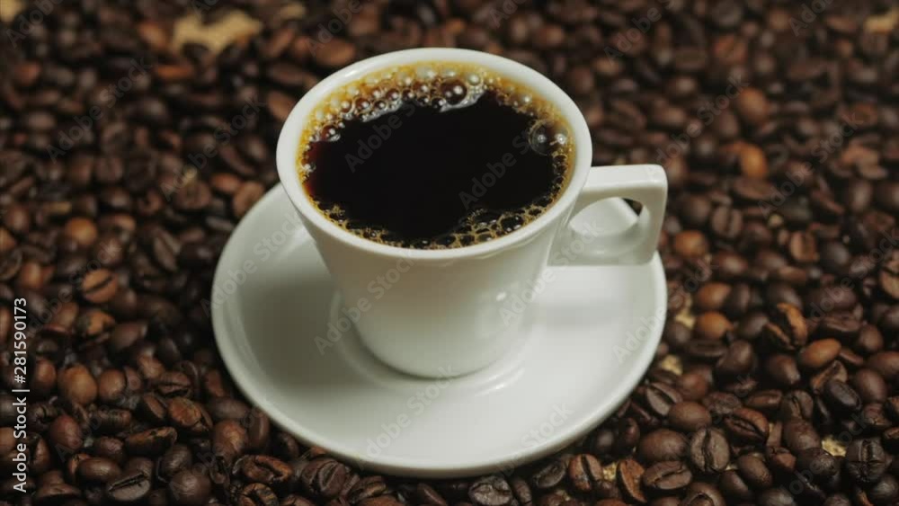 Coffee cup and coffee beans. White cup of evaporating coffee on the table with roasted bean. Stock footage. Coffee cup and coffee beans. White cup of evaporating coffee on the table with roasted bean. Stock footage.