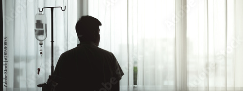 Silhouette adult patient stand and hold infusion hanger pole look out to hospital window, thinking about medical expenses and health care insurance alone, financial and wellness problem concept. photo