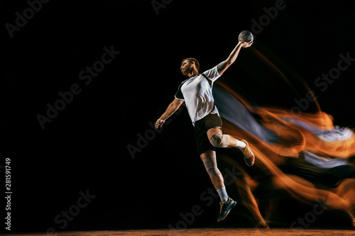 Caucasian young handball player in action and motion in mixed lights over black studio background. Fit male professional sportsman. Concept of sport, movement, energy, dynamic, healthy lifestyle.