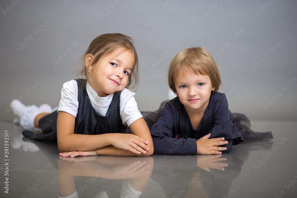 Two beautiful girls of the little sister pose lying on a gray background Two beautiful girls of the little sister pose lying on a gray background