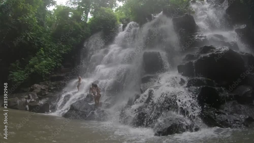 Three young friends are standing on rocks under a big waterfall to get their photo and video taken. Three young friends are standing on rocks under a big waterfall to get their photo and video taken.