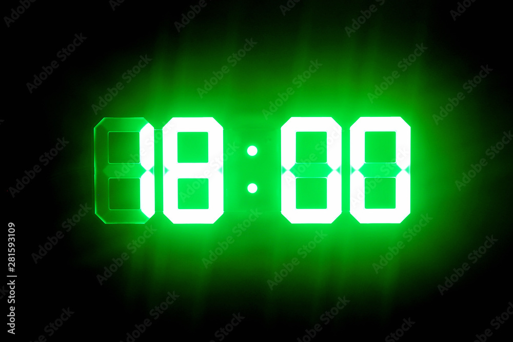Green glowing digital clocks in the dark show 18:00 time