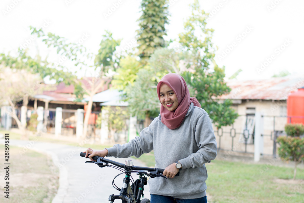 portrait of beautiful asian muslim woman wearing hijab riding a bike